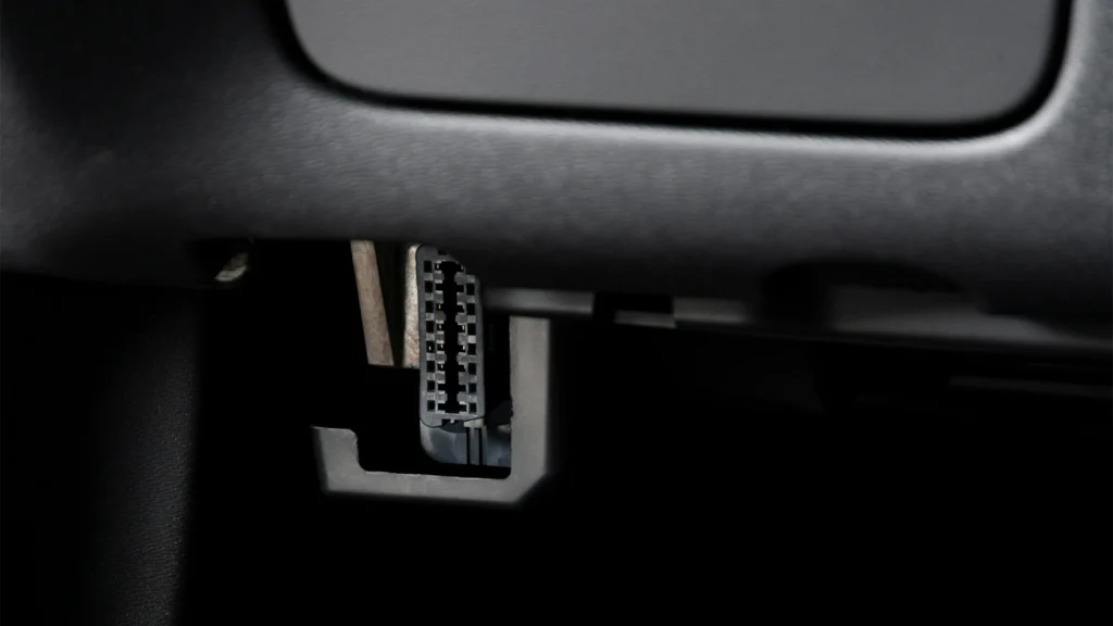 A close-up of a vehicle's OBD-II port, illustrating the simple plug-and-play installation for a GPS tracker.