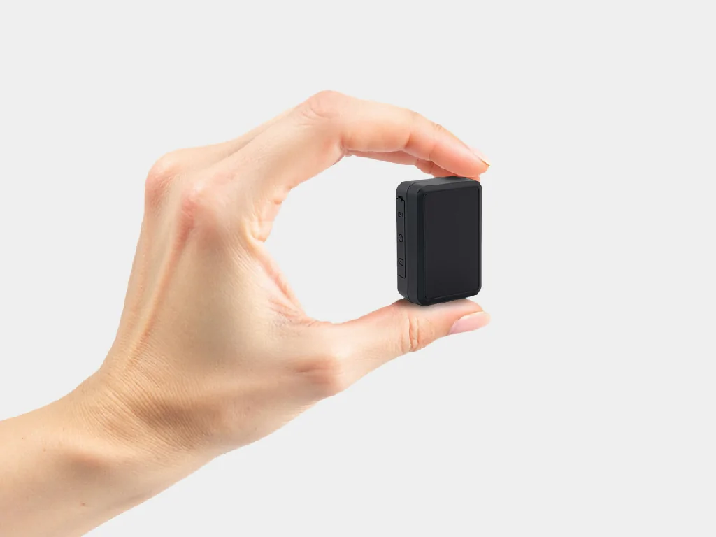 A hand holding the ultra-compact GAT27 personal GPS tracker to demonstrate its small, discreet size.
