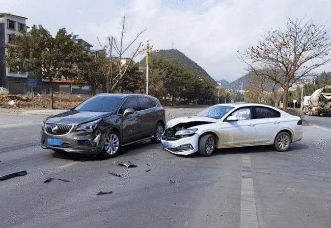 The scene of a road accident where a white sedan and a grey SUV have collided, resulting in severe front-end damage and debris on the road.